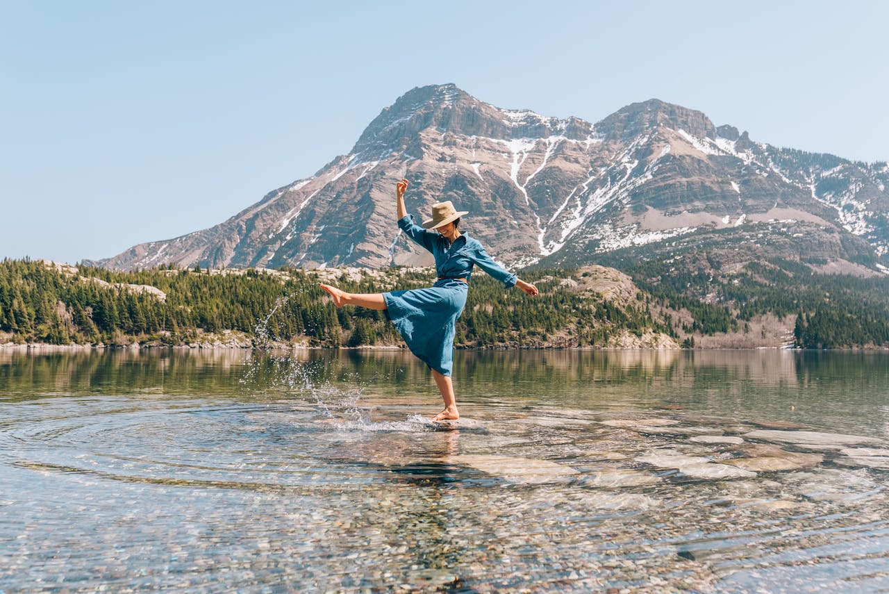 Woman smiling and kicking water in the middle of a lake, mid-hike in a scenic mountainous region