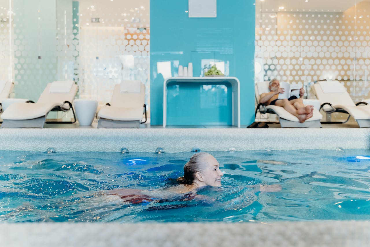 Woman swimming in a pool with lounge chairs and a blue wall in the background