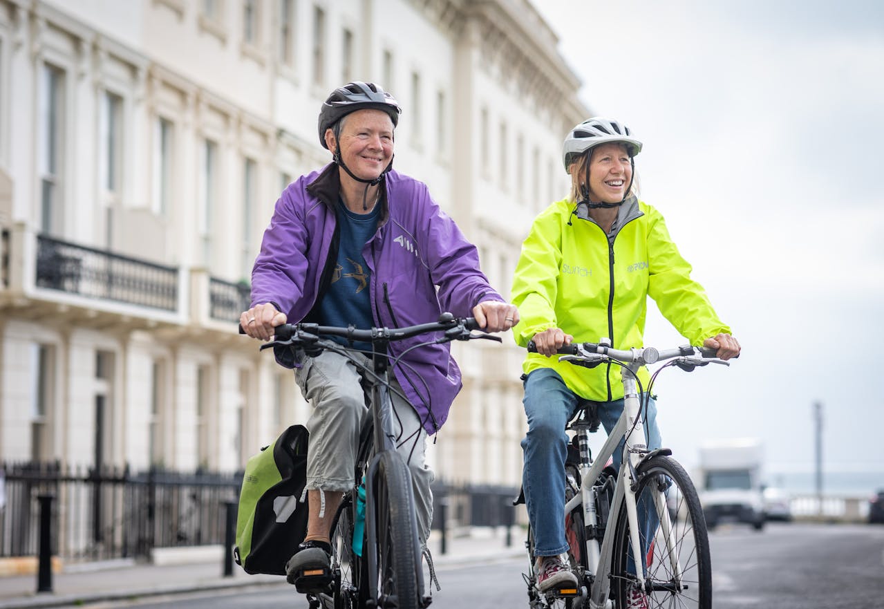 Two seniors riding bicycles on a city street with buildings in the background