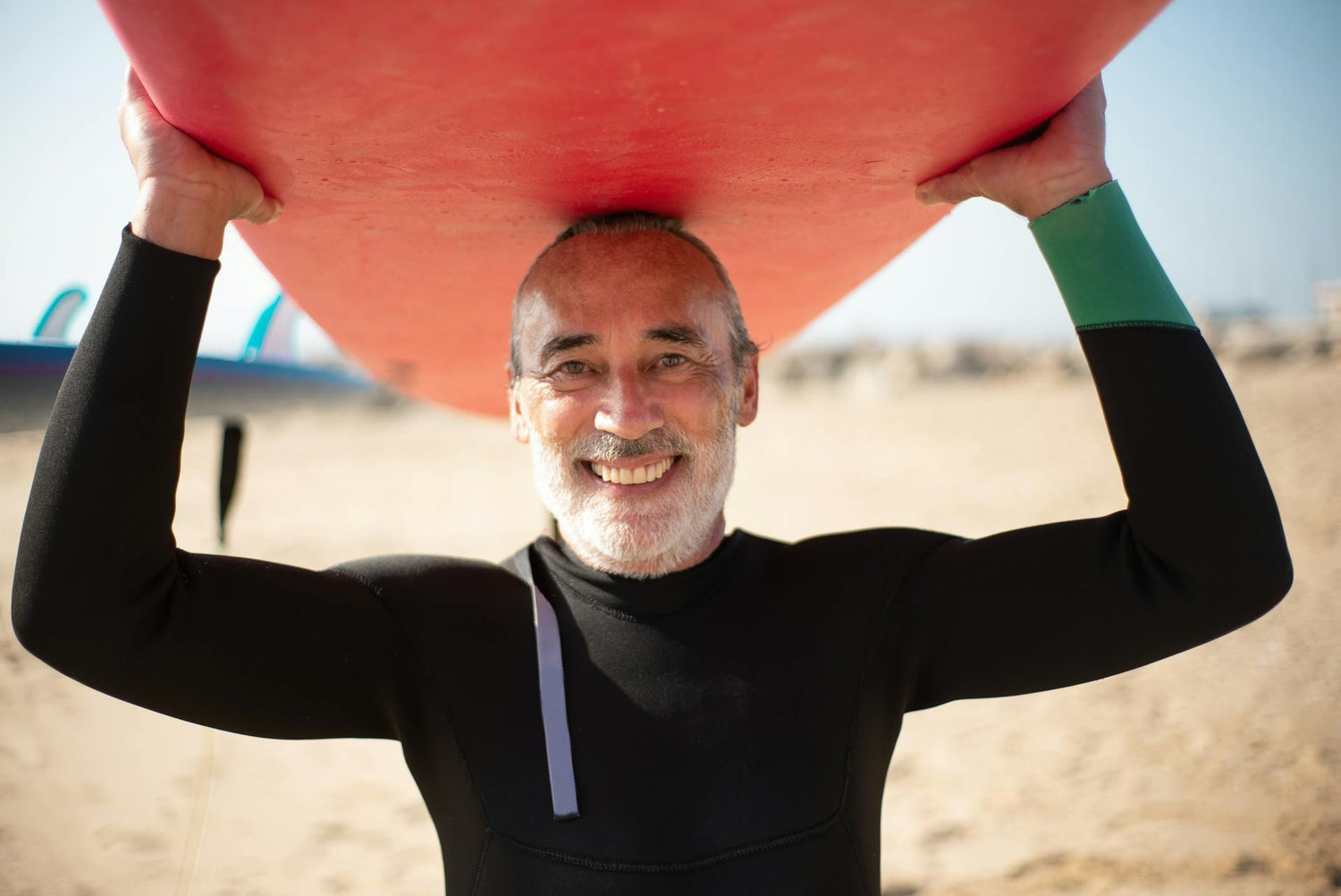 Man in a wetsuit holding a red surfboard on a beach